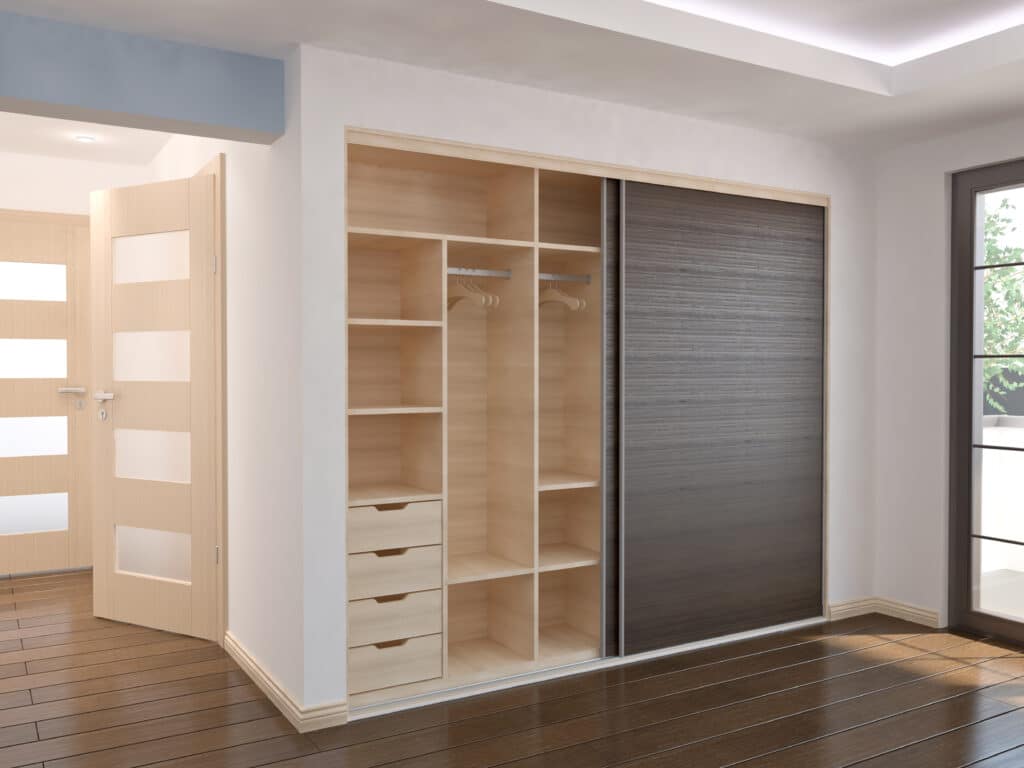 Grande armoire intégrée bois clair et gris foncé, portes coulissantes. Plancher bois sombre, portes vitrées, murs blancs. Intérieur moderne.